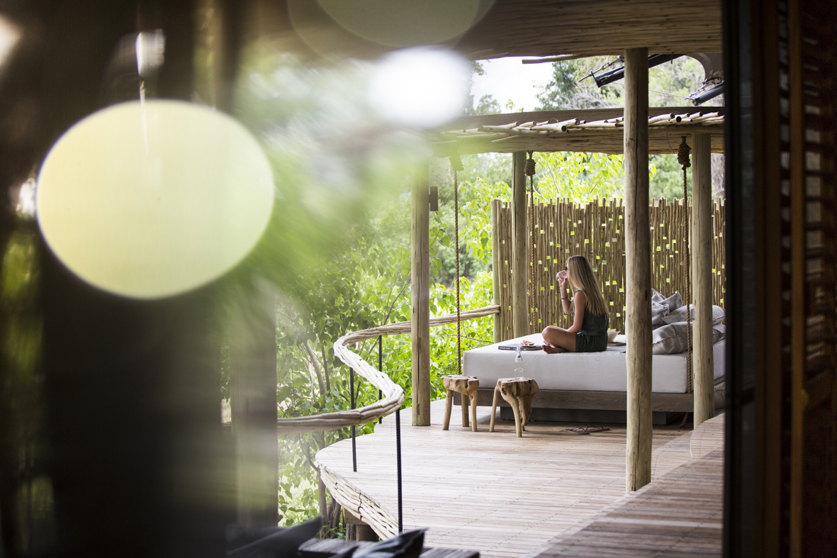 Wilderness, Little Mombo, Botswana. Women enjoying the serenity of her private veranda and day bed