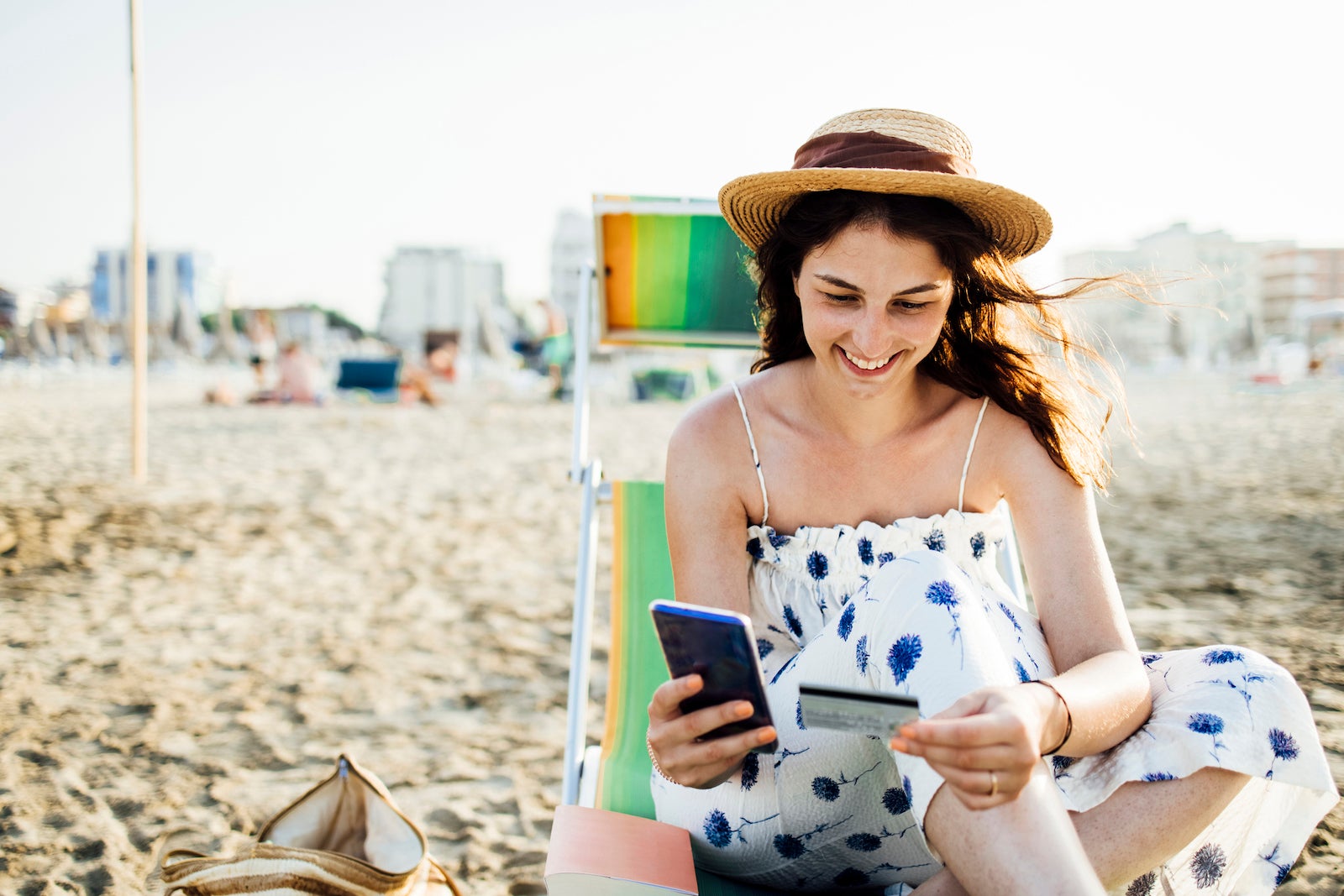 tourist on a beach uses credit card and smart phone to shop online