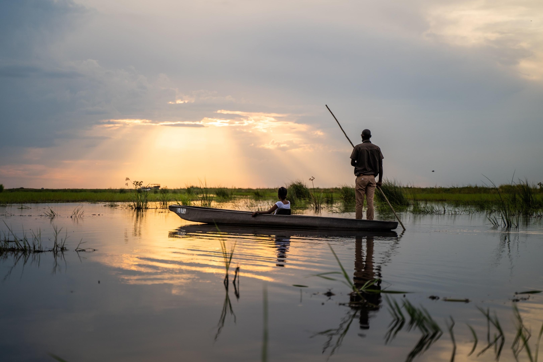 African-Bush-Camps-Linyanti-Ebony-botswana-safari-mokoro A guide poles a traditional mokoro canoe through the calm waters of the Okavango Delta at sunset, offering a serene perspective on why this is the best time to visit Botswana for a safari.