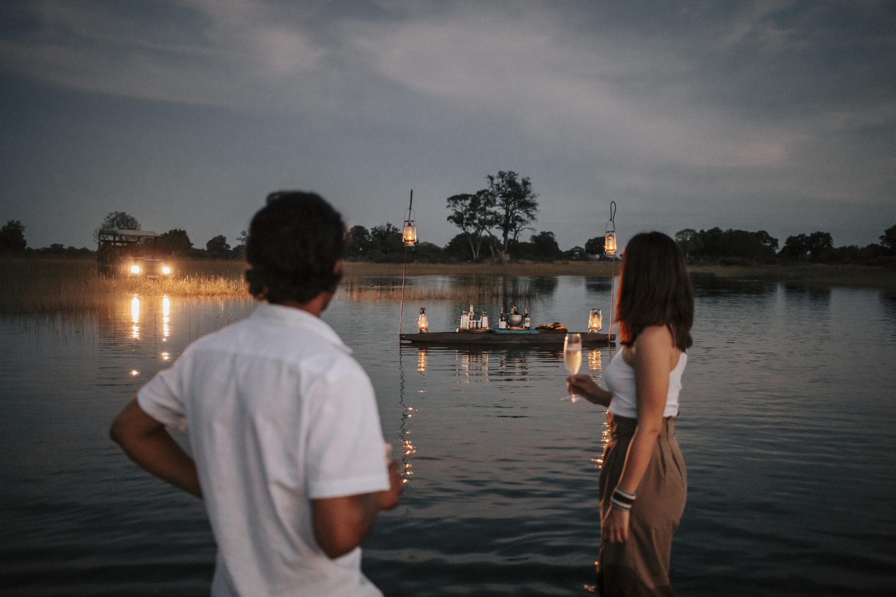 Wilderness Vumbura Plains_3 A couple stands ankle-deep in water, champagne in hand, gazing at a floating lantern-lit bar in the Okavango Delta—an unforgettable way to enjoy the best time to visit Botswana for a safari.